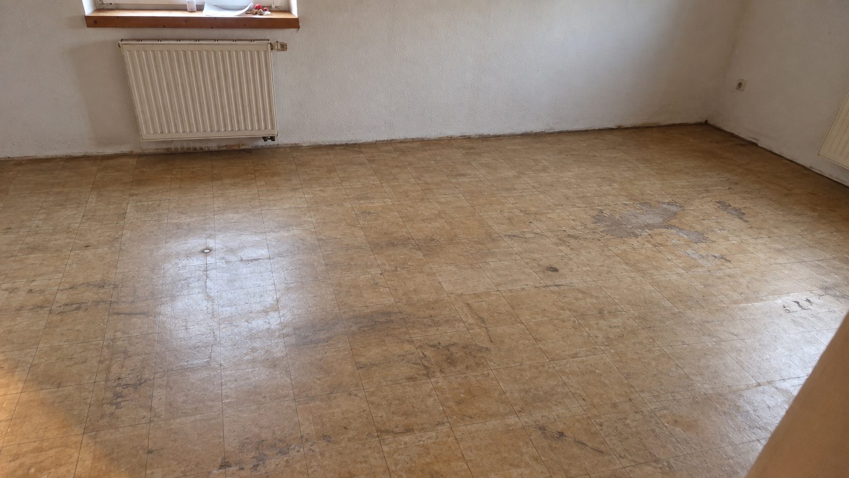 Vor der Arbeit: abgenutzter, fleckiger Altbelag mit Klebstoffresten im leeren Zimmer